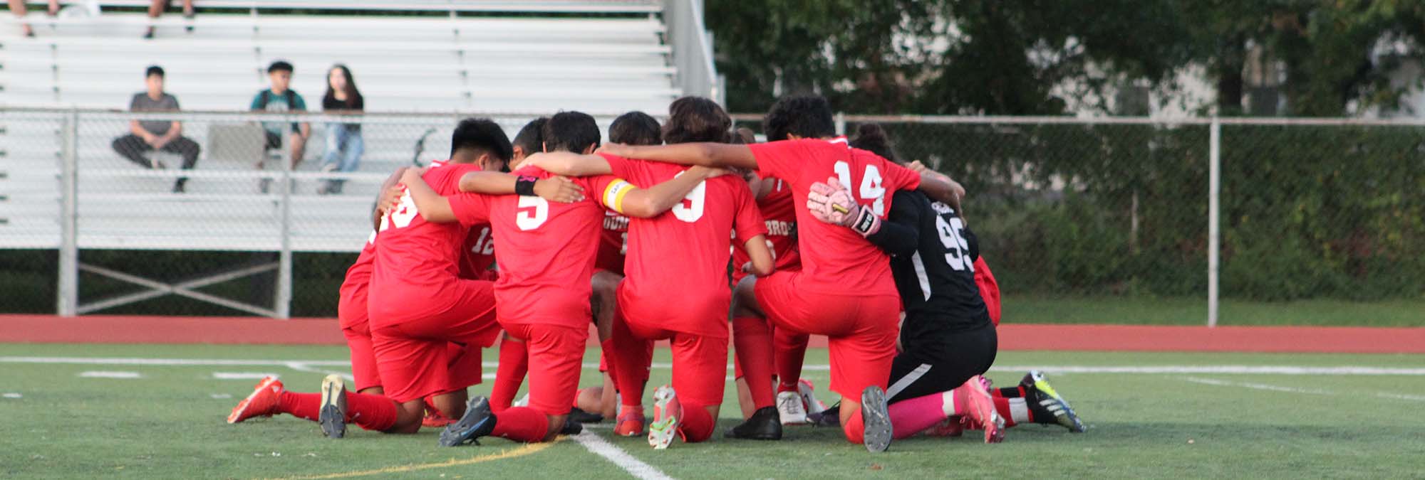 BBHS soccer players kneel in a circle on field