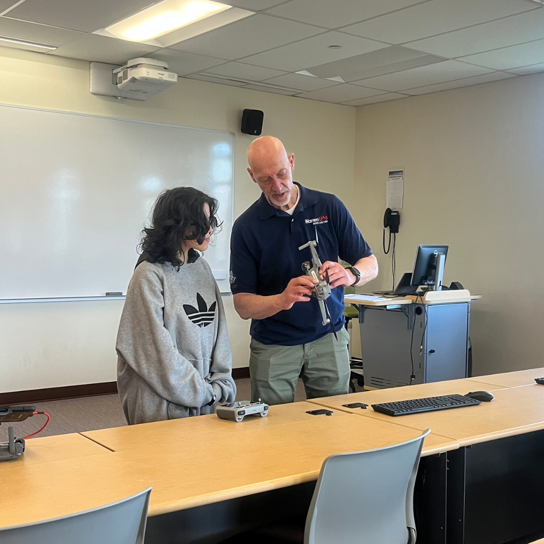 A student inspects a drone for flying in a classroom with the instructor.